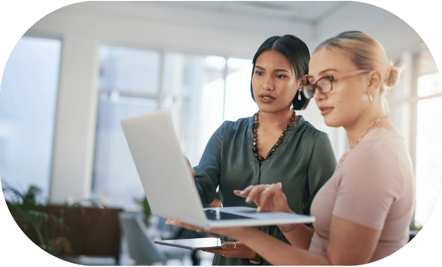 Two coworkers conversing and looking at a laptop